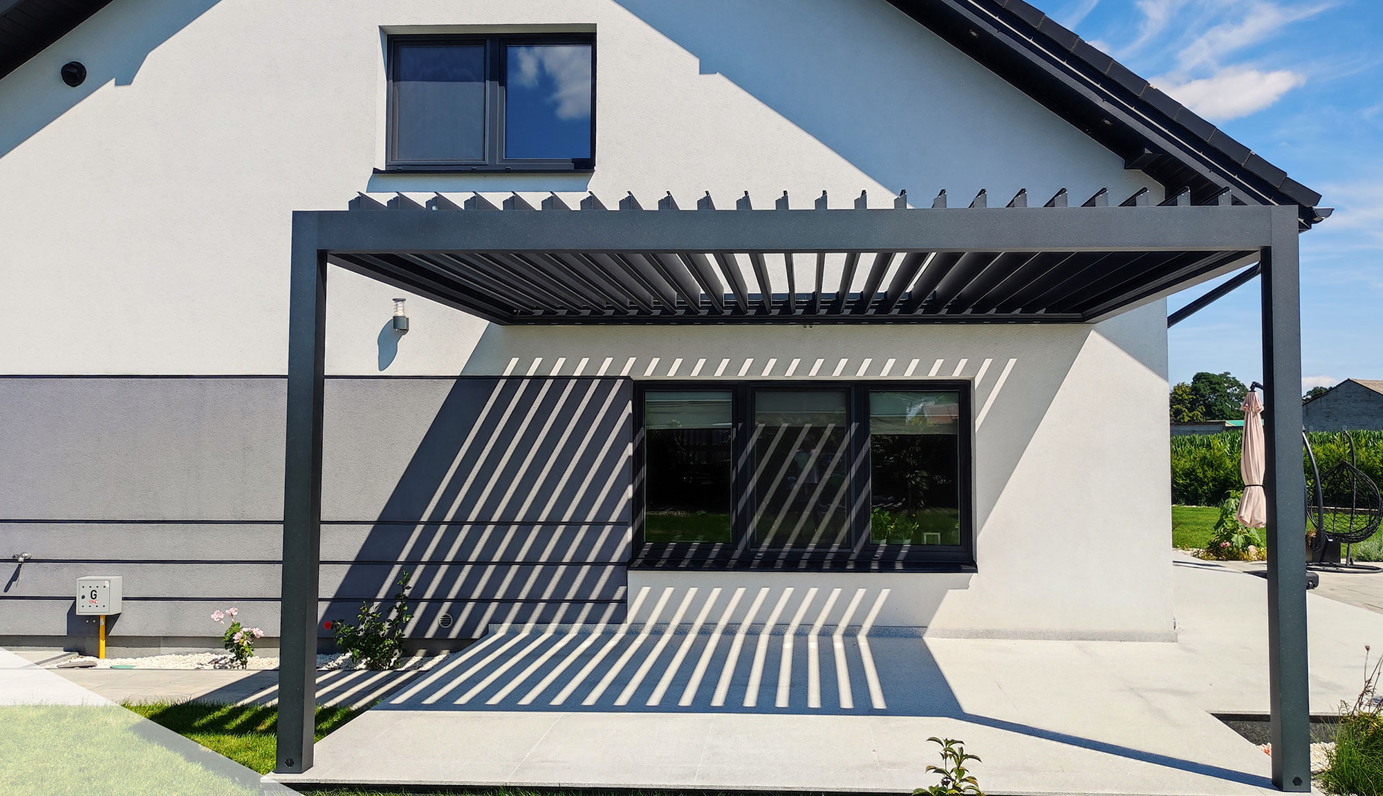 Anthrazites Lamellendach an ein modernes Wohnhaus angebaut. Vorne mit zwei Säulen. Die Lamellen stehen aufrecht und sich auch anthrazit.