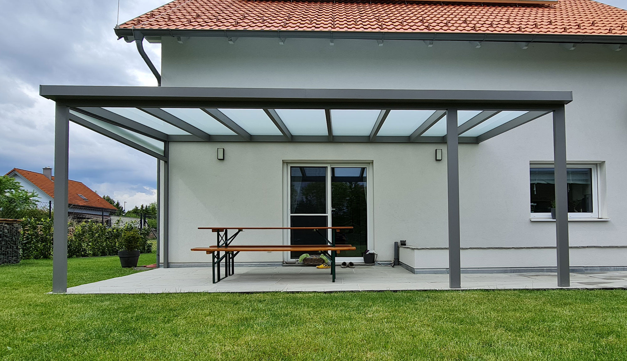 Graue Terrassenüberdachung mit Glaseindeckung ohne Erweiterungen. Das Glas ist opal, also undurchsichtig.